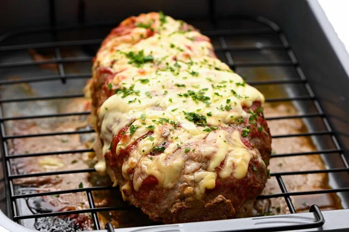 Stuffed meatloaf on baking rack over pan topped with cheese.