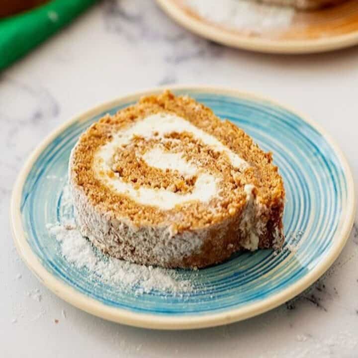 Slice of homemade pumpkin roll with cream cheese filling on blue plate.