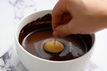 Peanut Butter ball with toothpick dipping into melted chocolate.