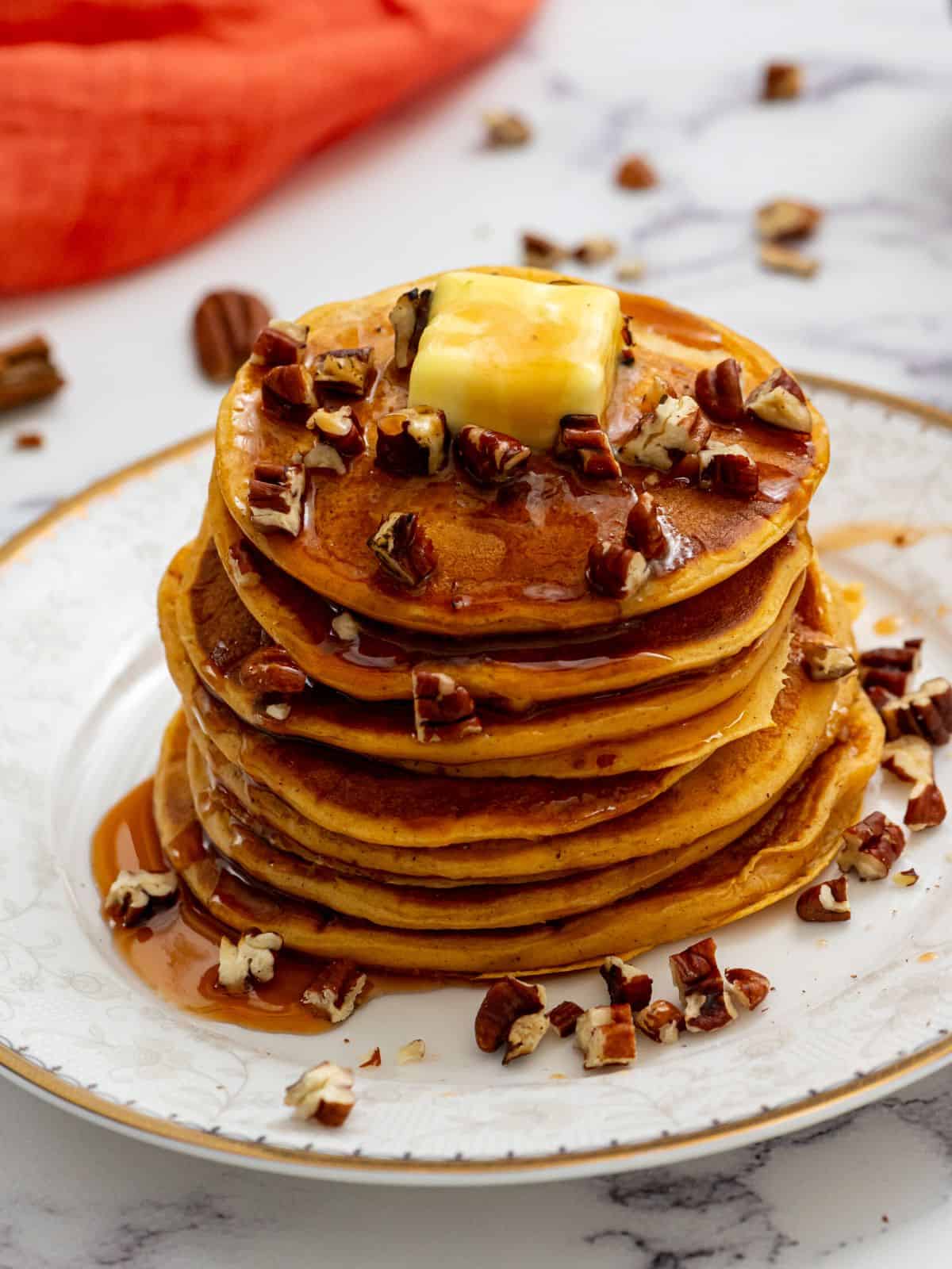 Stack of sweet potato pancakes on plate topped with maple syrup and chopped nuts.
