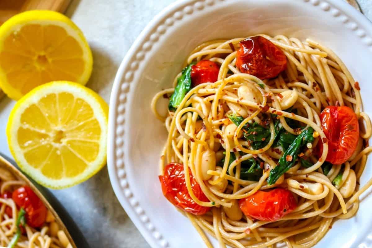 Close up of bowl with tuscan pasta next to fresh lemons.