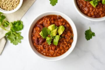 Lentil Chili dished up in white bowl topped with avocado and cilantro.