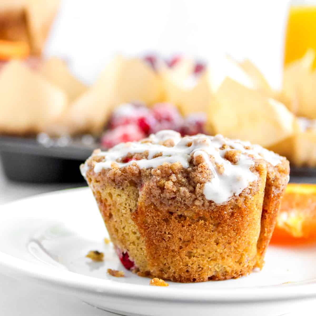 Cranberry Orange Muffin on white plate with glaze and streusel and orange slices in background.