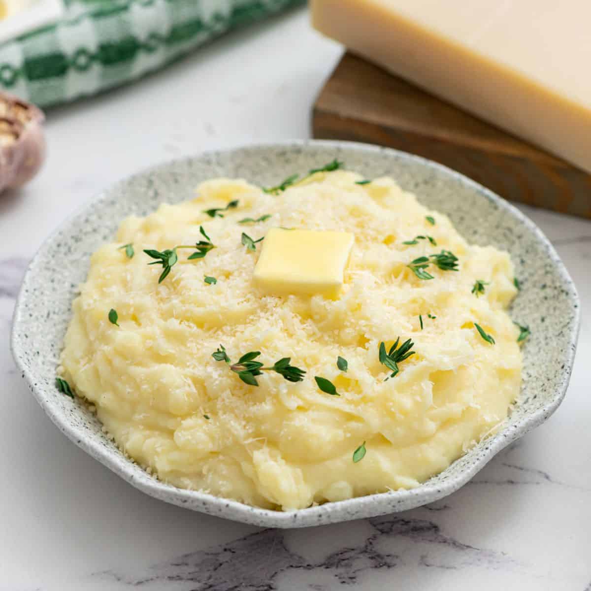 Crockpot mashed potatoes in serving bowl topped with parmesan, butter, and thyme.