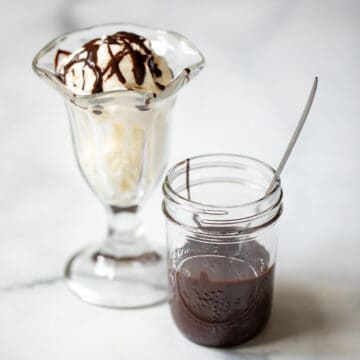 Jar of homemade chocolate syrup next to vanilla ice cream sundae.