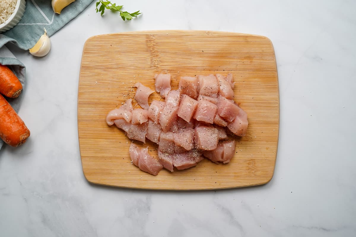 Diced chicken on cutting board seasoned with salt and pepper.