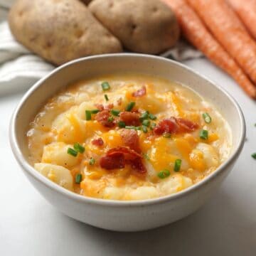 Bowl of instant pot baked potato soup topped with cheese, bacon and chives.