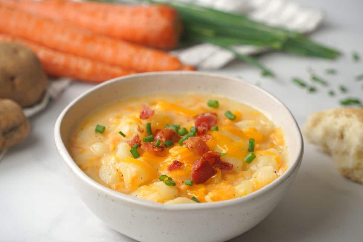 Bowl of instant pot baked potato soup topped with cheese, bacon and chives.
