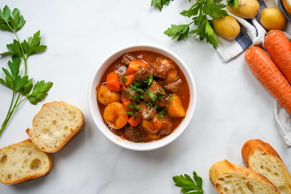 Bowl of instant pot beef stew topped with parsley next to sliced bread.