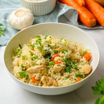 Bowl of instant pot chicken and rice in white bowl topped with parsley.