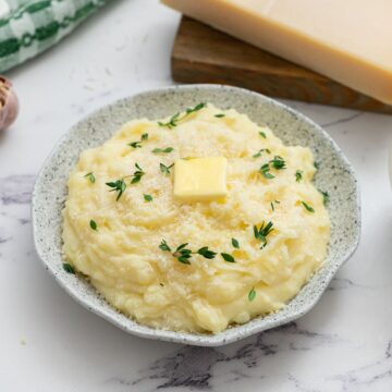 Crockpot mashed potatoes in serving bowl topped with parmesan, butter, and thyme.