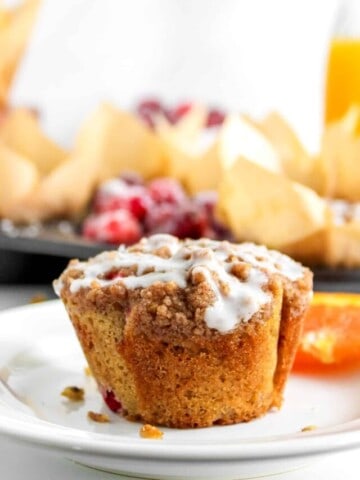 Baked Cranberry Orange Muffins on white plate next to fresh orange.