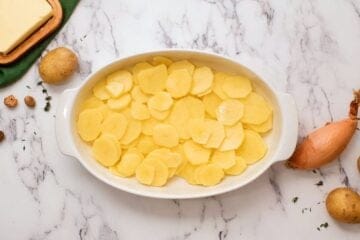 Sliced yukon gold potatoes in white casserole dish.