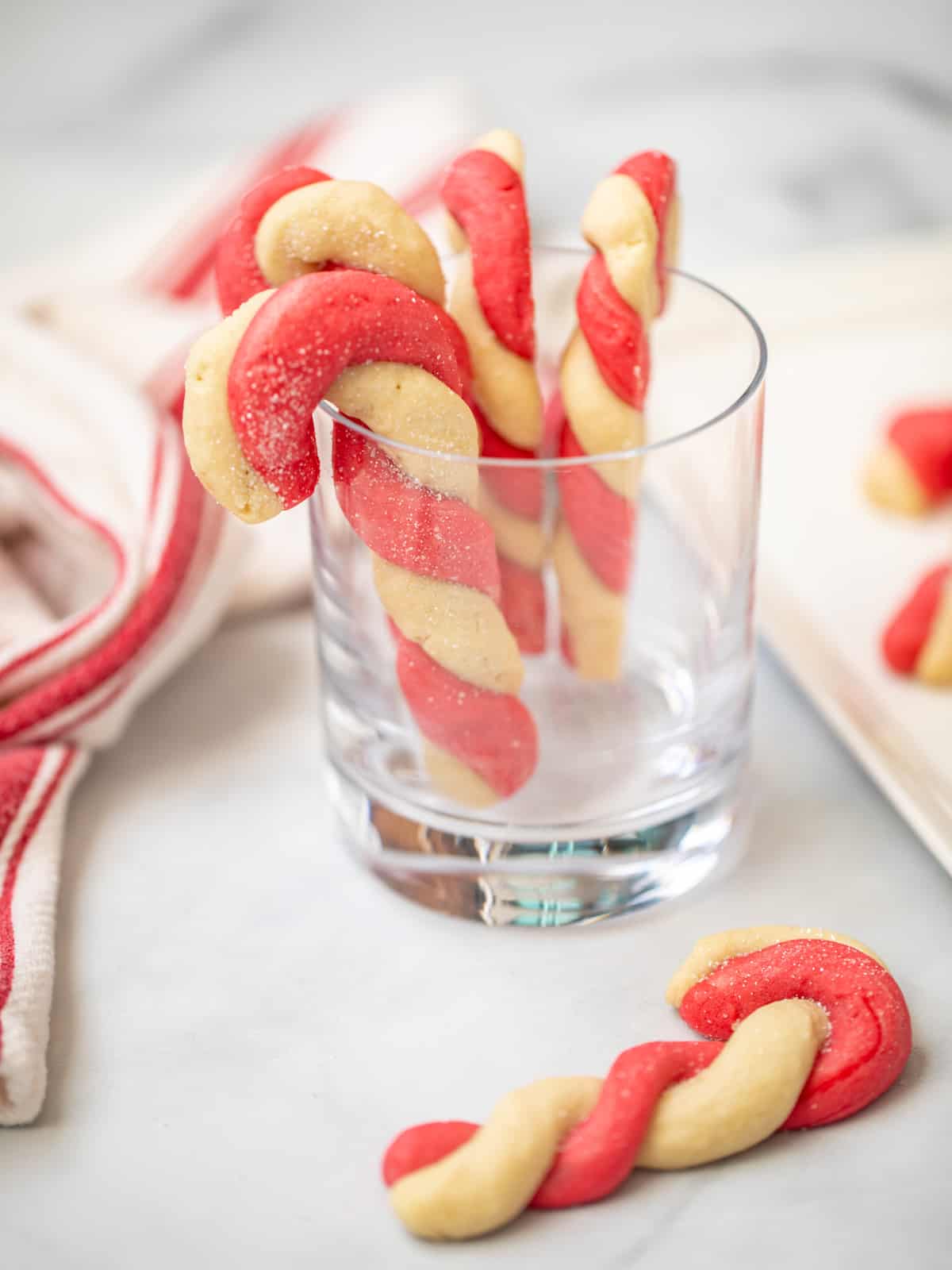 Candy Cane cookies hanging on a clear drinking glass with baked cookie in front of the glass.