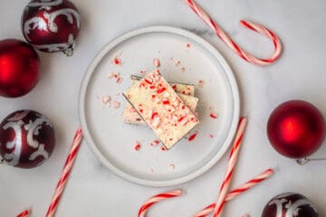 Homemade Peppermint Bark cut in rectangles on plate next to christmas ornaments and candy canes.