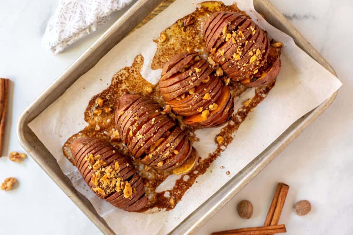 Baked hasselback sweet potatoes topped with nuts on baking sheet.