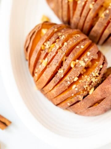 Top down view of maple-glazed hasselback sweet potato on white platter.