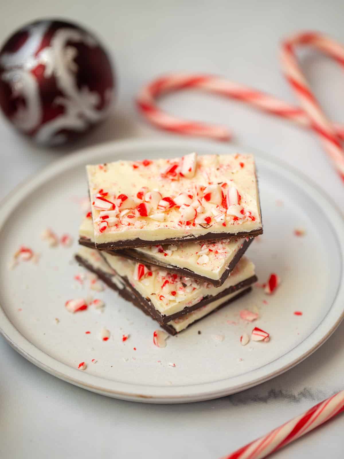 Peppermint Bark on plate stack up with candy canes in background.