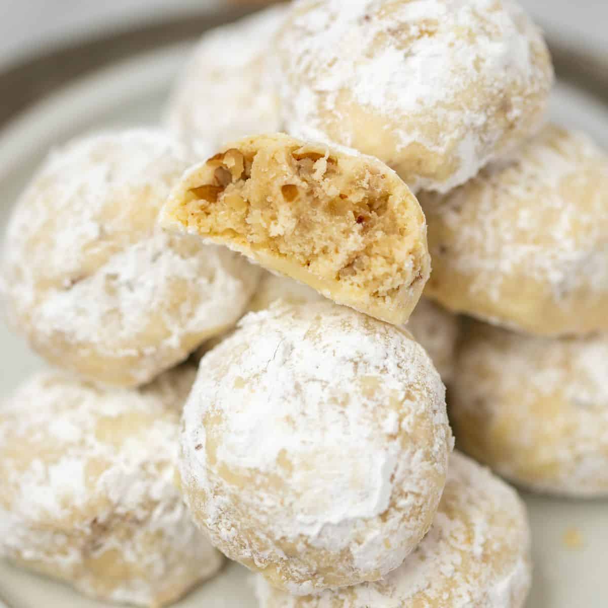 Close up of snowball of cookies cut open showing pecans and light interior of cookies.