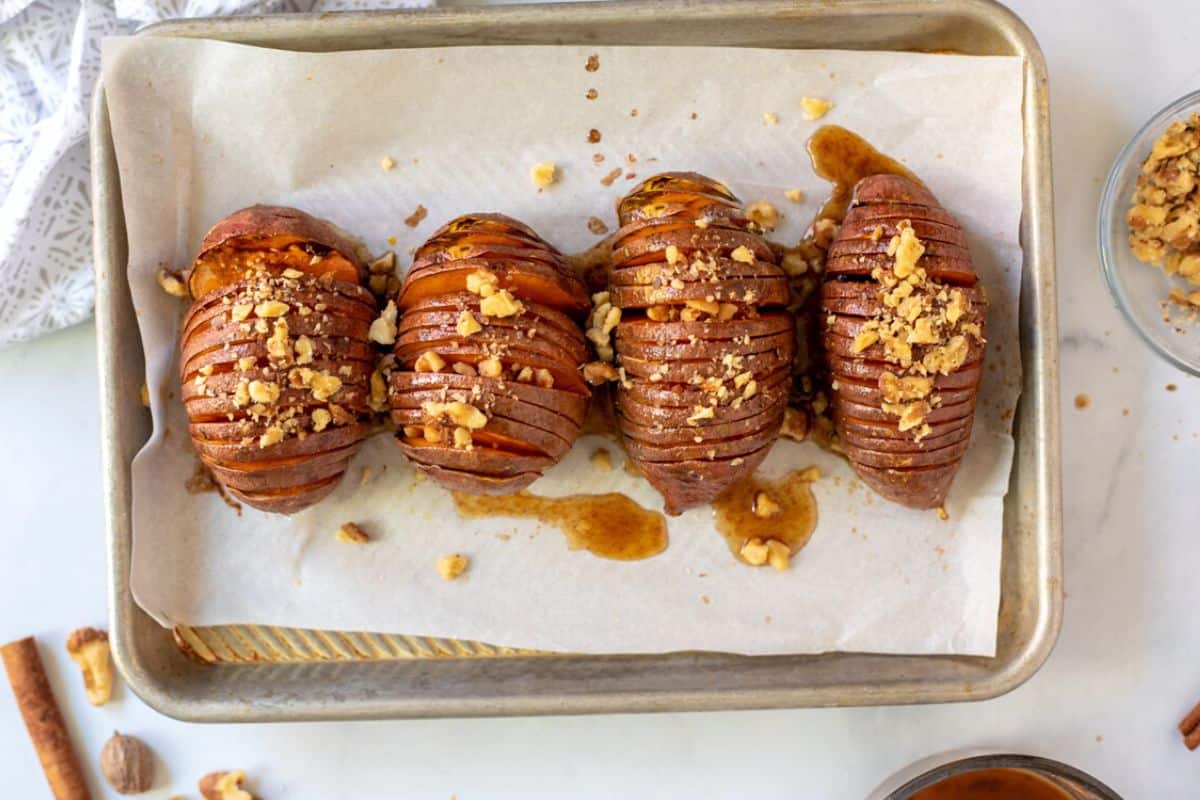 Hasselback sweet potatoes on tray after being glazed and topped with nuts.
