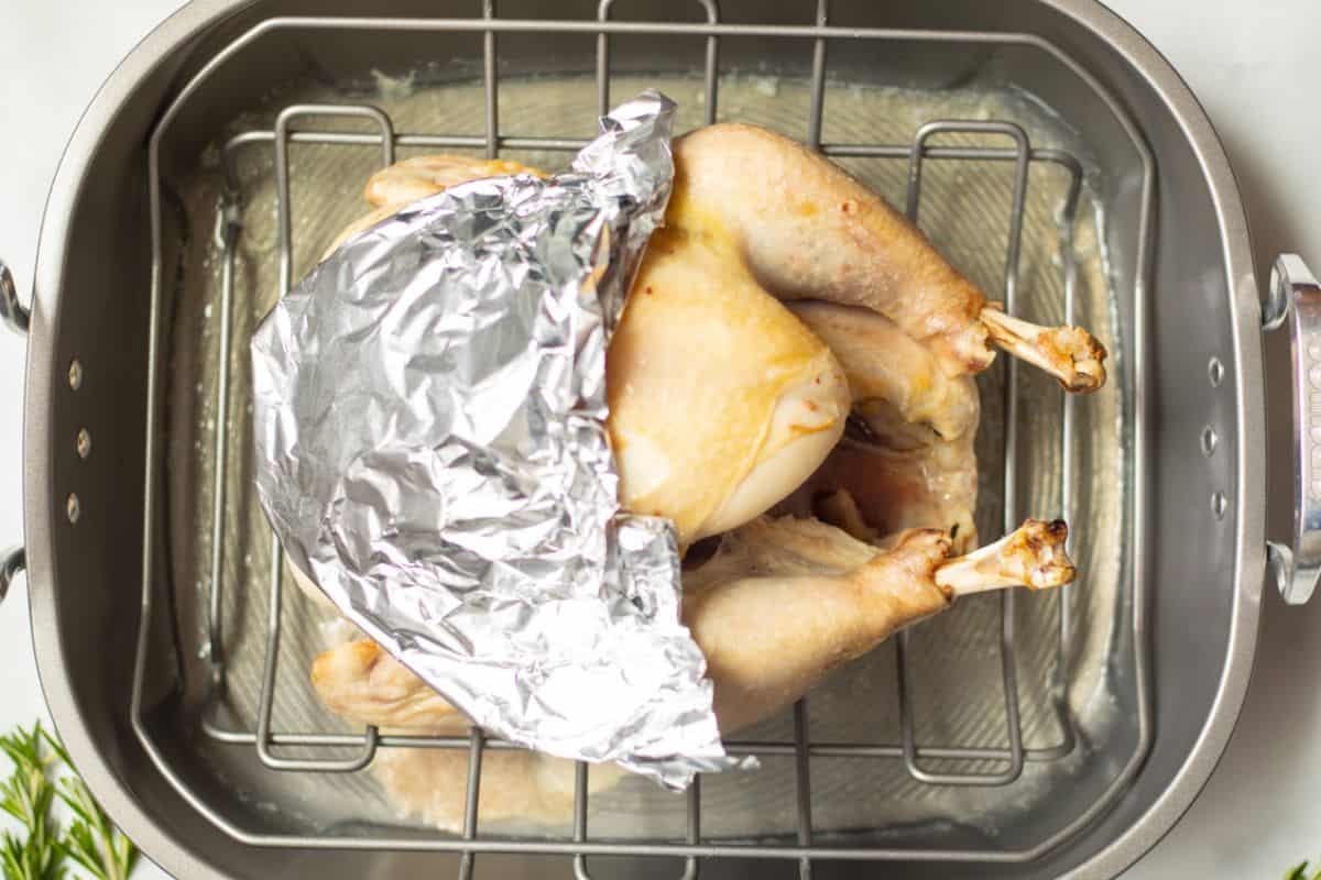 Partially cooked turkey in roasting pan with foil covering just the breasts.
