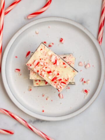 Peppermint Bark on plate stack up with candy canes in background.