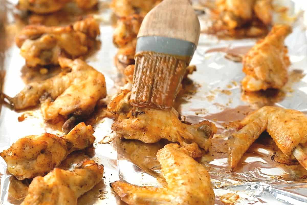 Pastry brush brushing chicken wings with buffalo sauce.