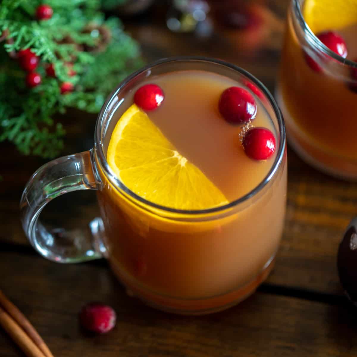Top down view of glass of spiced Christmas tea served with wedge of an orange and fresh cranberries.