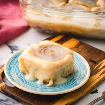 Healthy Cinnamon Roll on blue serving plate with tray of cinnamon rolls in background.