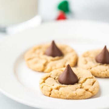 Baked peanut butter blossom cookies on white plate with glass of milk in backgrond.