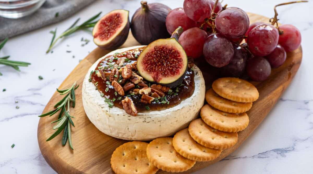 Baked Brie on cutting board with crackers, figs, and walnuts.