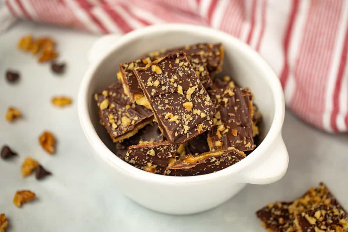 Bowl of saltine cracker toffee with walnuts and chocolate chips on counter.