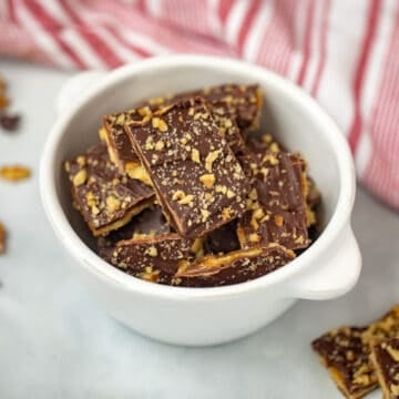Bowl of saltine cracker toffee with walnuts and chocolate chips on counter.