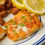 Baked Cod with butter and lemon wedges on plate with blue stripes.