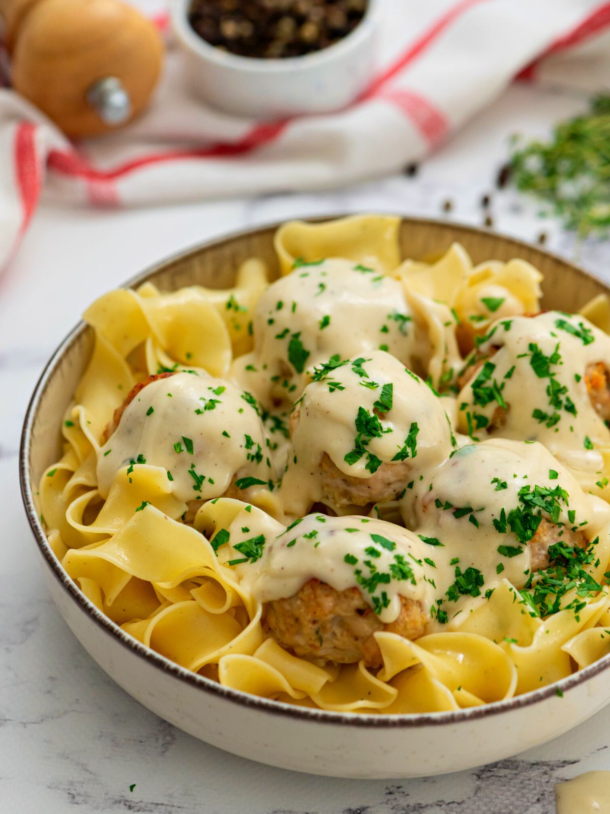 Bowl of Swedish meatballs served over egg noodles and topped with parsley.