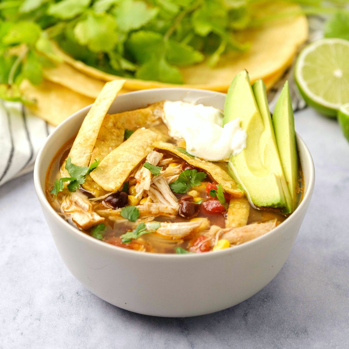 Instant Pot Chicken Tortilla Soup in bowl topped with homemade toritlla strips, sour cream, and sliced avocado.