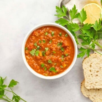 Bowl of lentil soup topped with fresh parsley next to sliced bread.