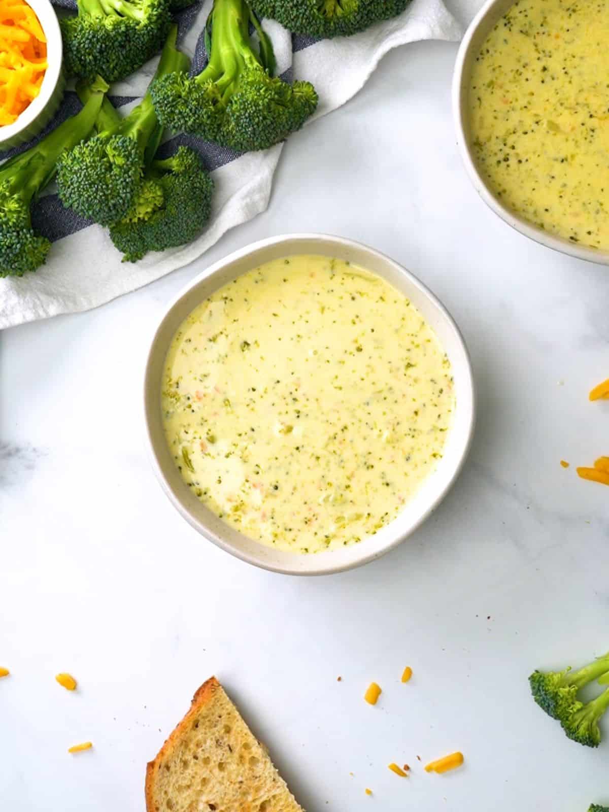 Bowl of instant pot broccoli cheddar soup next to crusty bread and instant pot.