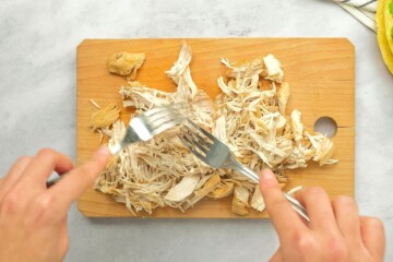 Showing 2 forks shredded chicken on cutting board.