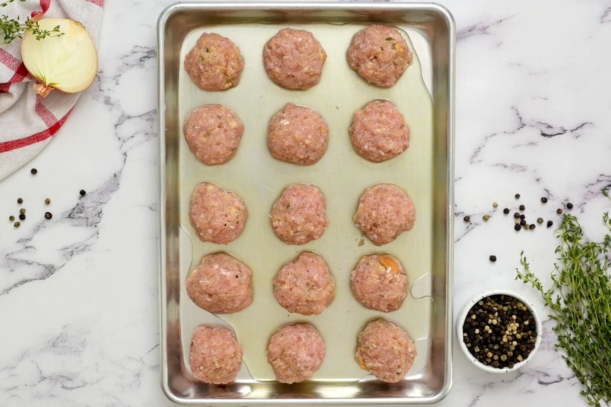 Turkey Meatballs shaped on sheet pan with chicken stock poured around the meatballs.