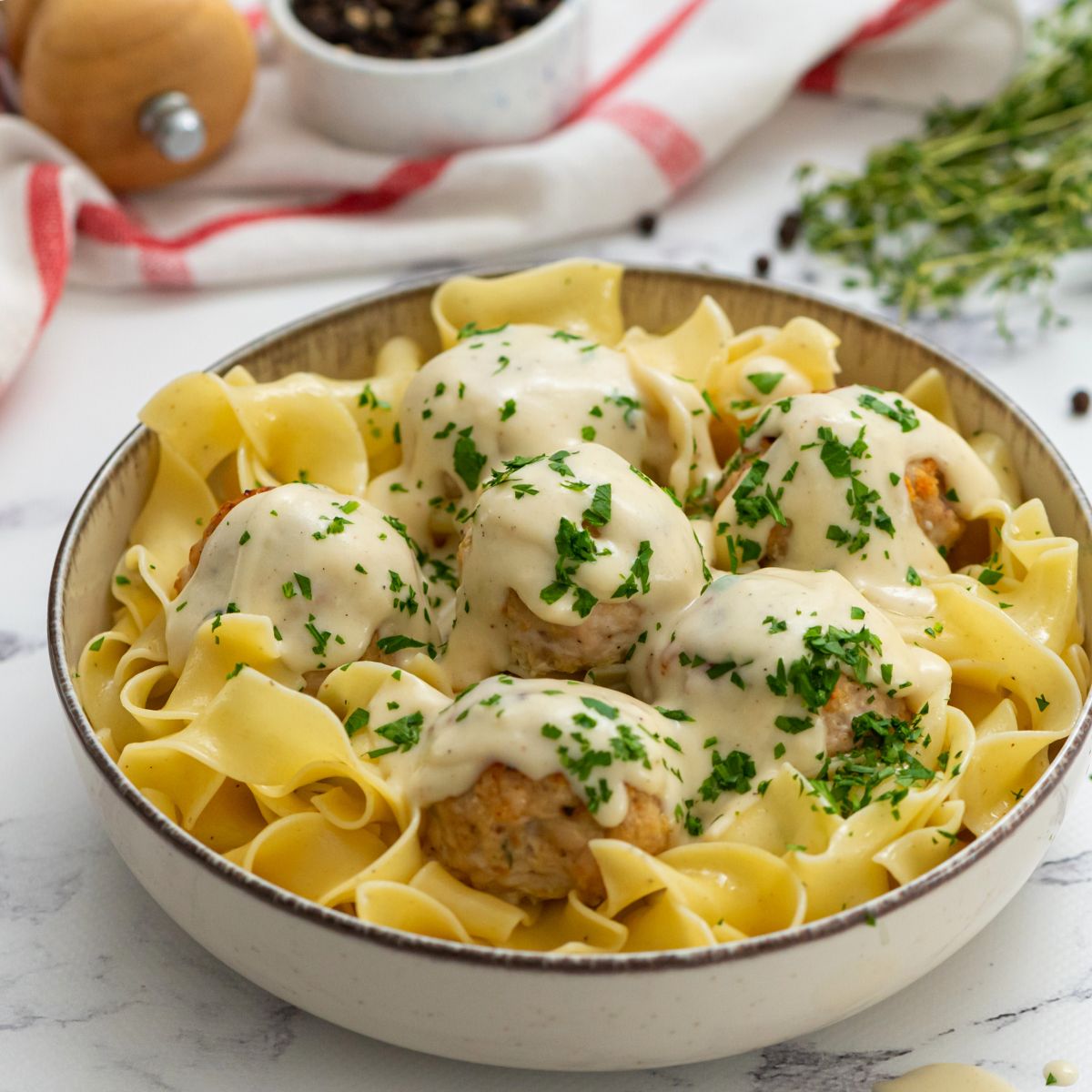 Bowl of Swedish meatballs served over egg noodles and topped with parsley.