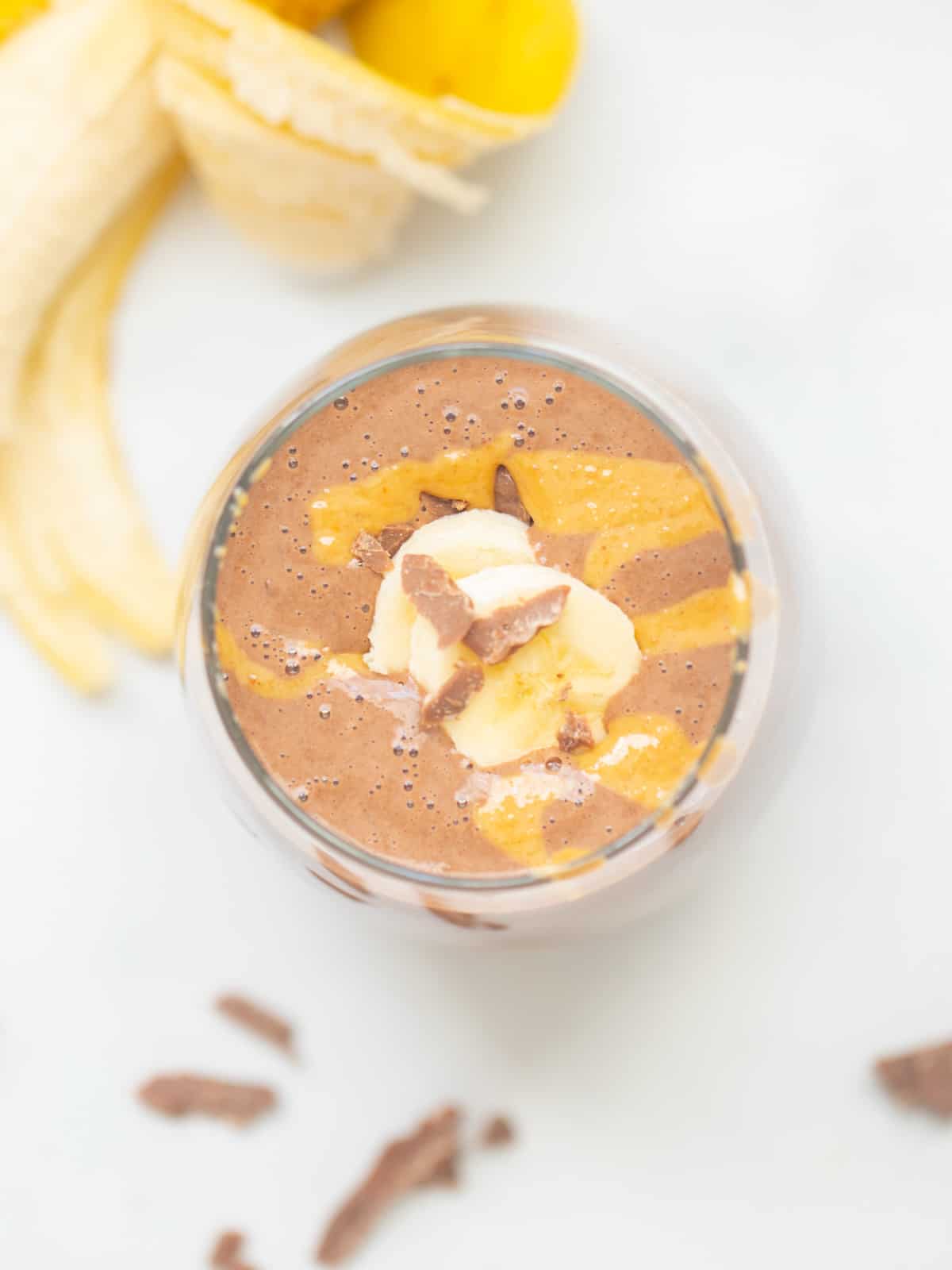 Top down view of chocolate peanut butter smoothie in glass topped with peanut butter, chocolate, and sliced banana.