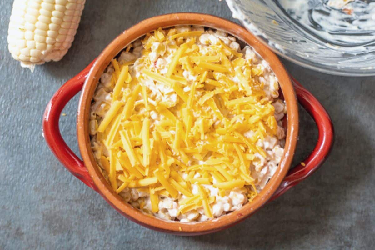 Corn dip in red crock topped with shredded cheddar cheese.