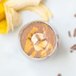 Top down view of chocolate peanut butter smoothie in glass topped with peanut butter, chocolate, and sliced banana.