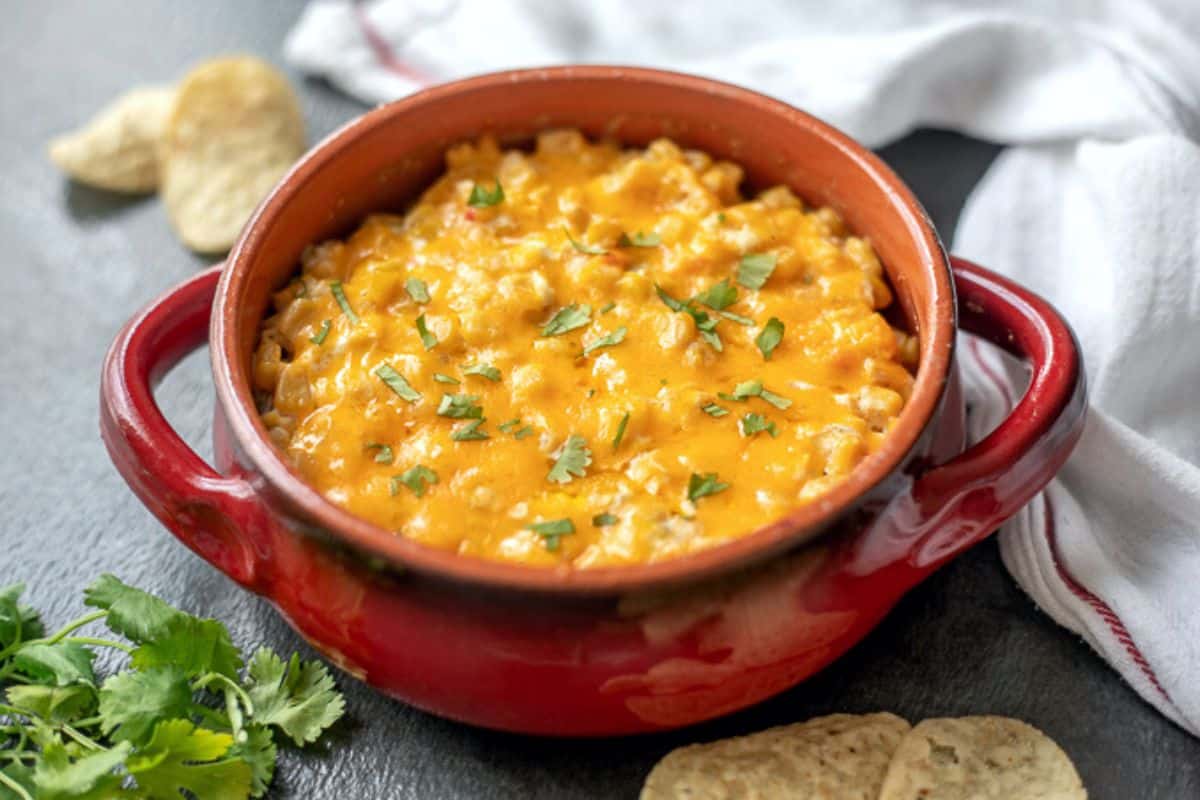 Warm corn dip in red bowl next to tortilla chips.