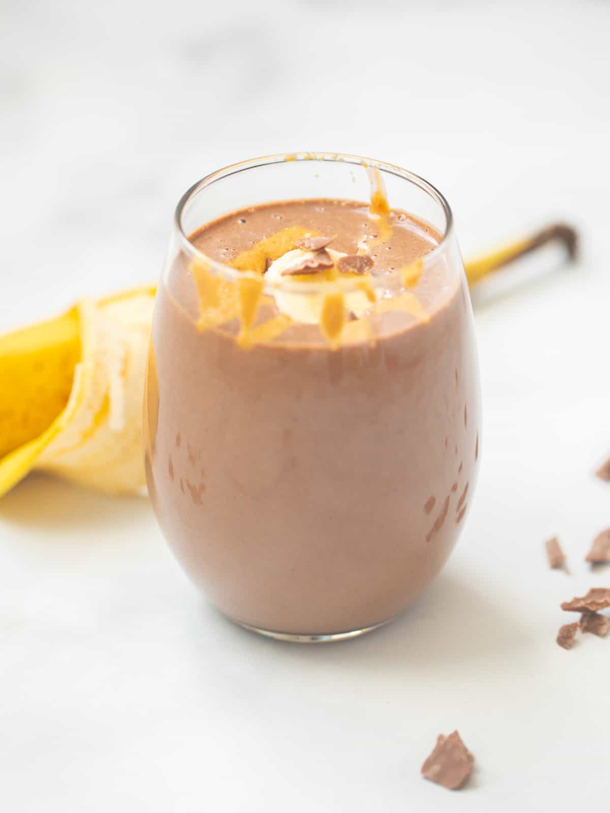 Peanut Butter Chocolate smoothie in clear glass topped with sliced banana, drizzle peanut butter, and chocolate.