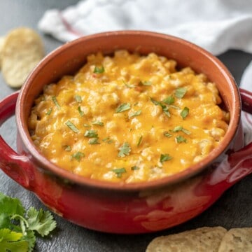 Warm corn dip in red bowl next to tortilla chips.