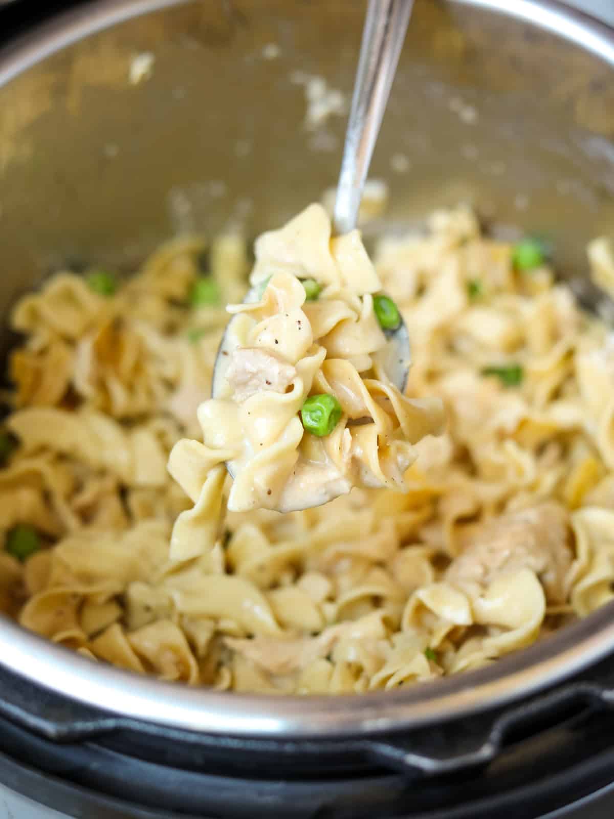 Spoon coming out of Instant Pot with noodles, tuna, and peas.