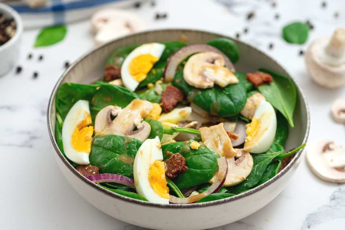 Spinach salad topped with bacon, mushrooms, red onions, and hard-boiled eggs.