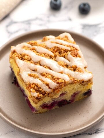Slice of blueberry Coffee Cake on a gray plate drizzled with lemon glaze.